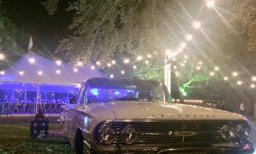 Voiture ancienne devant un chapiteau éclairé de guirlandes lumineuses